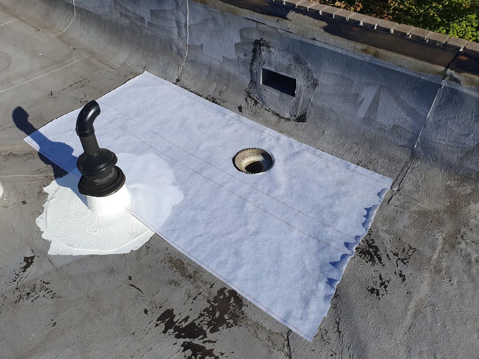 Reinforcement and silicone detail work around a commercial roof pipe, drain, and wall transition