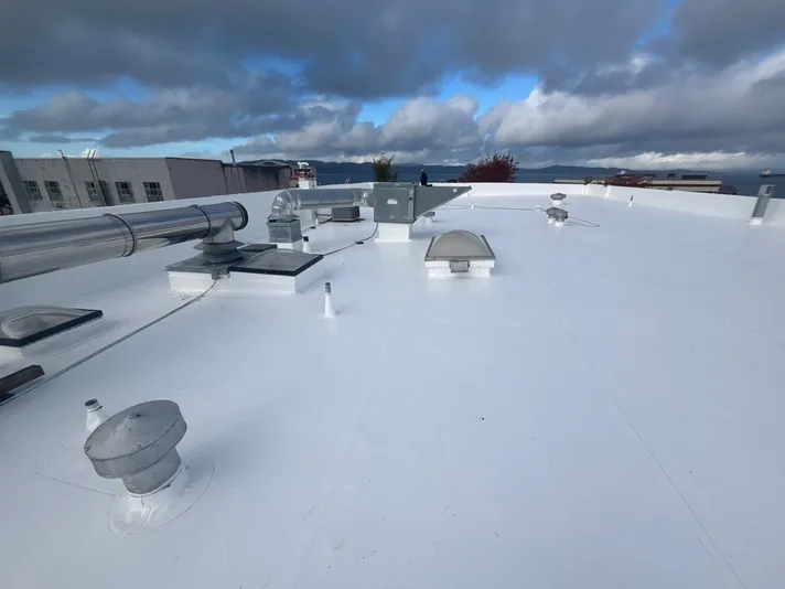 Completed commercial low-slope roof with a white membrane, vents, rooftop equipment, and sealed penetrations